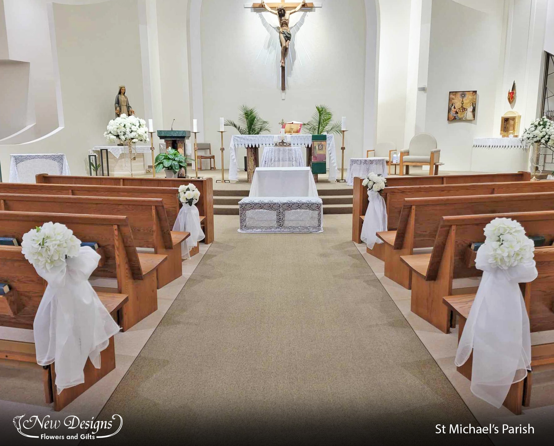 A modern church aisleway, the ends of the pews adorned with large bunches of white hydrangeas and roses with trailing White Organza material.